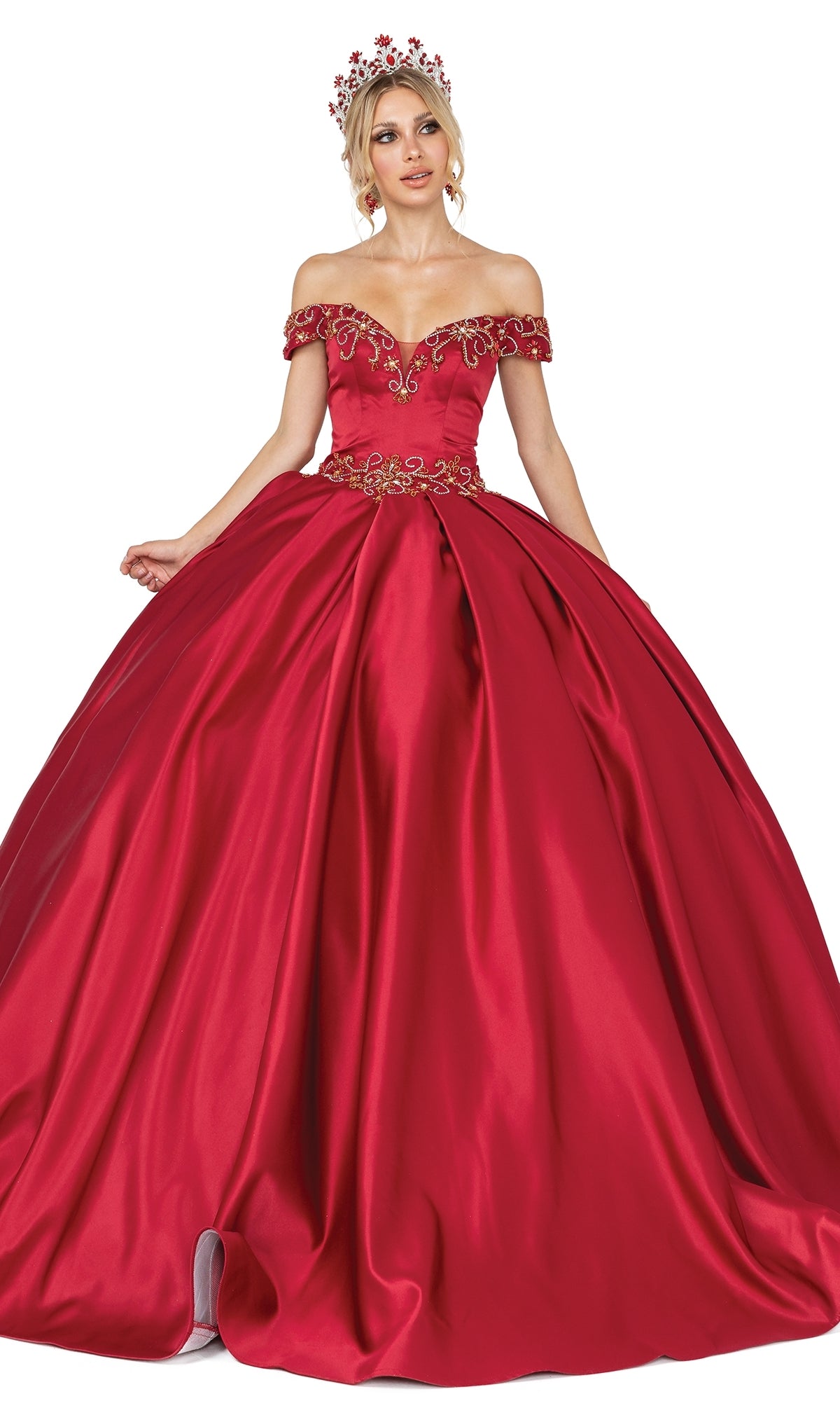 A woman wears the Quinceanera Dress 1466 by Dancing Queen, an off-the-shoulder, floor-length red A-line gown with gold embroidery and a matching red floral tiara, standing against a white background.